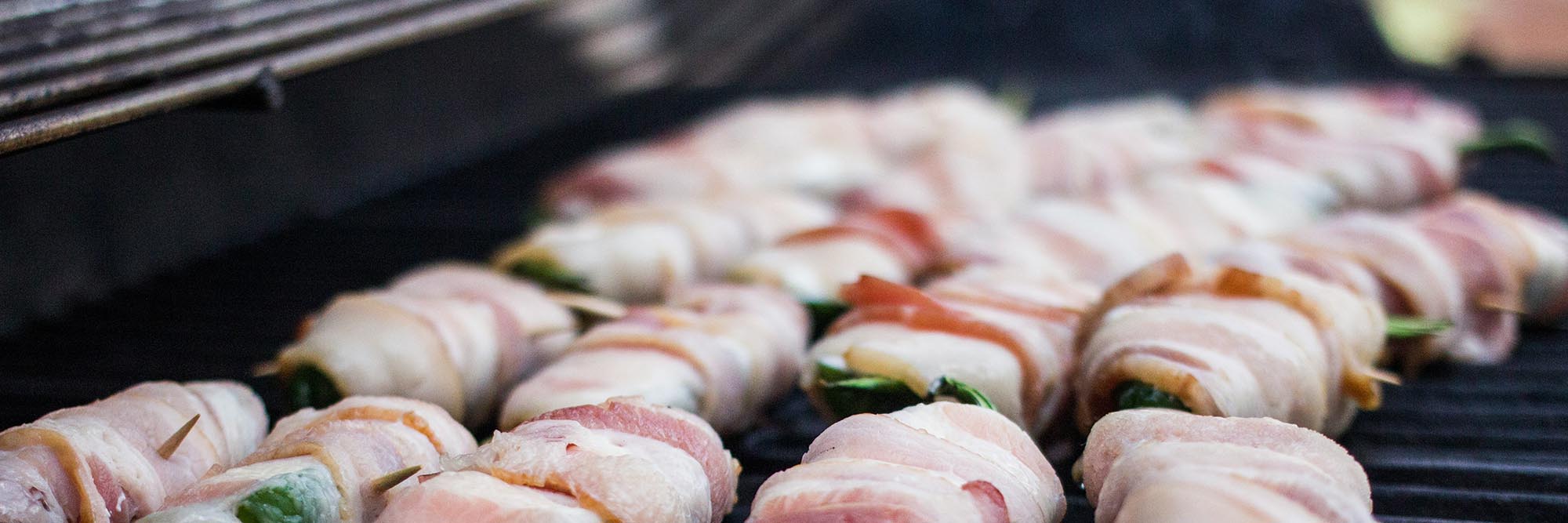 Baconrolletjes gevuld met groenten die langzaam garen op een grill tijdens het barbecueën.